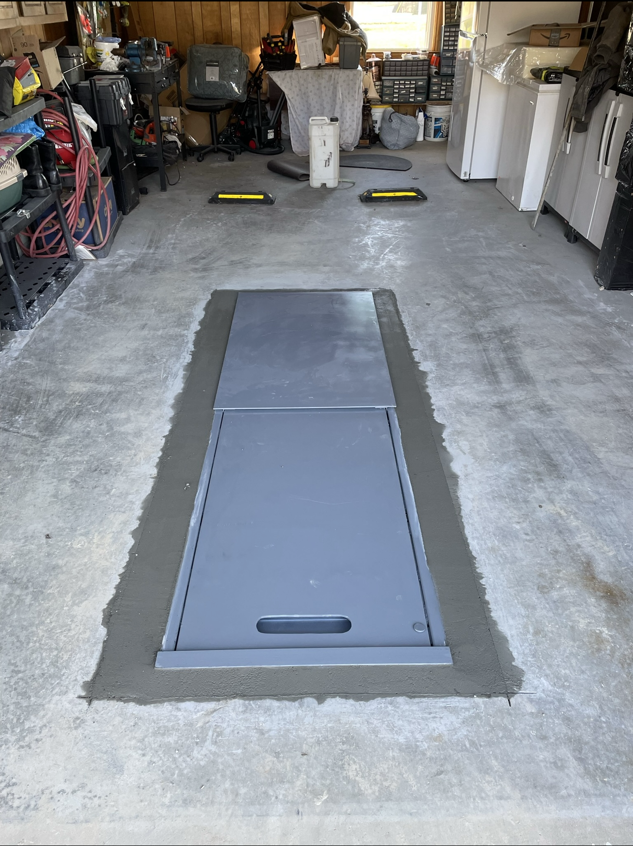 Garage with a gray metal in-ground lift and concrete perimeter, surrounded by tools and equipment.
