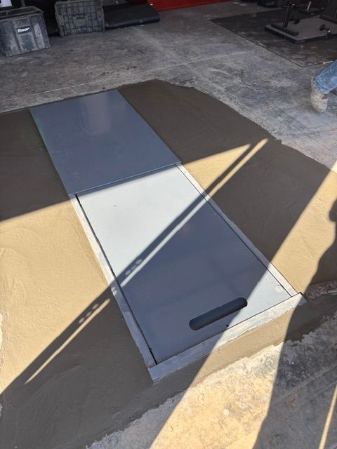 Gray metal access panel set into wet concrete floor.