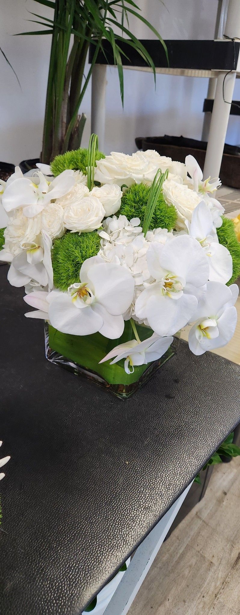 A vase filled with white flowers and greenery is sitting on a table.