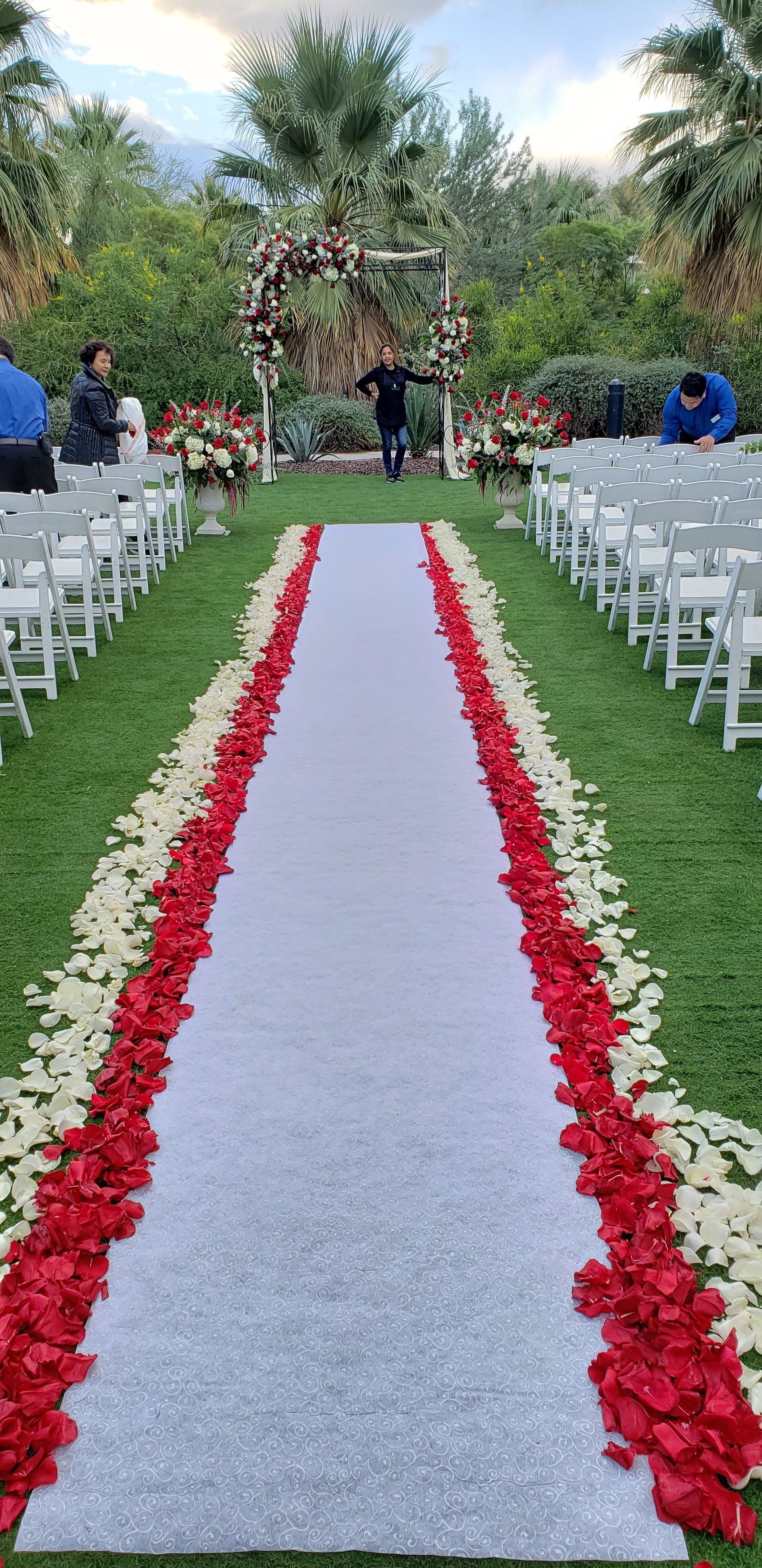 A wedding aisle decorated with red and white flowers and petals.