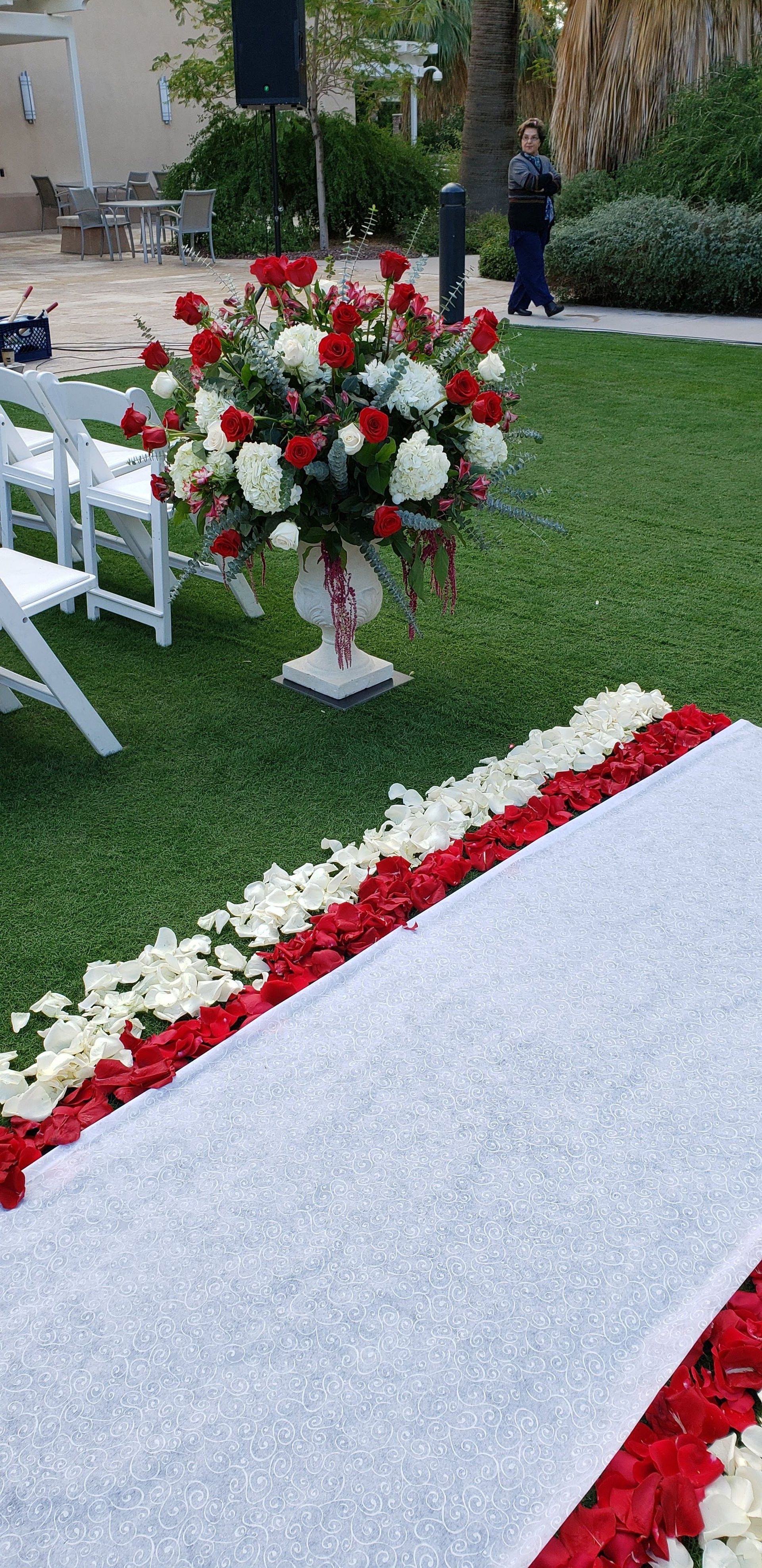 A wedding aisle decorated with red and white flowers and petals.
