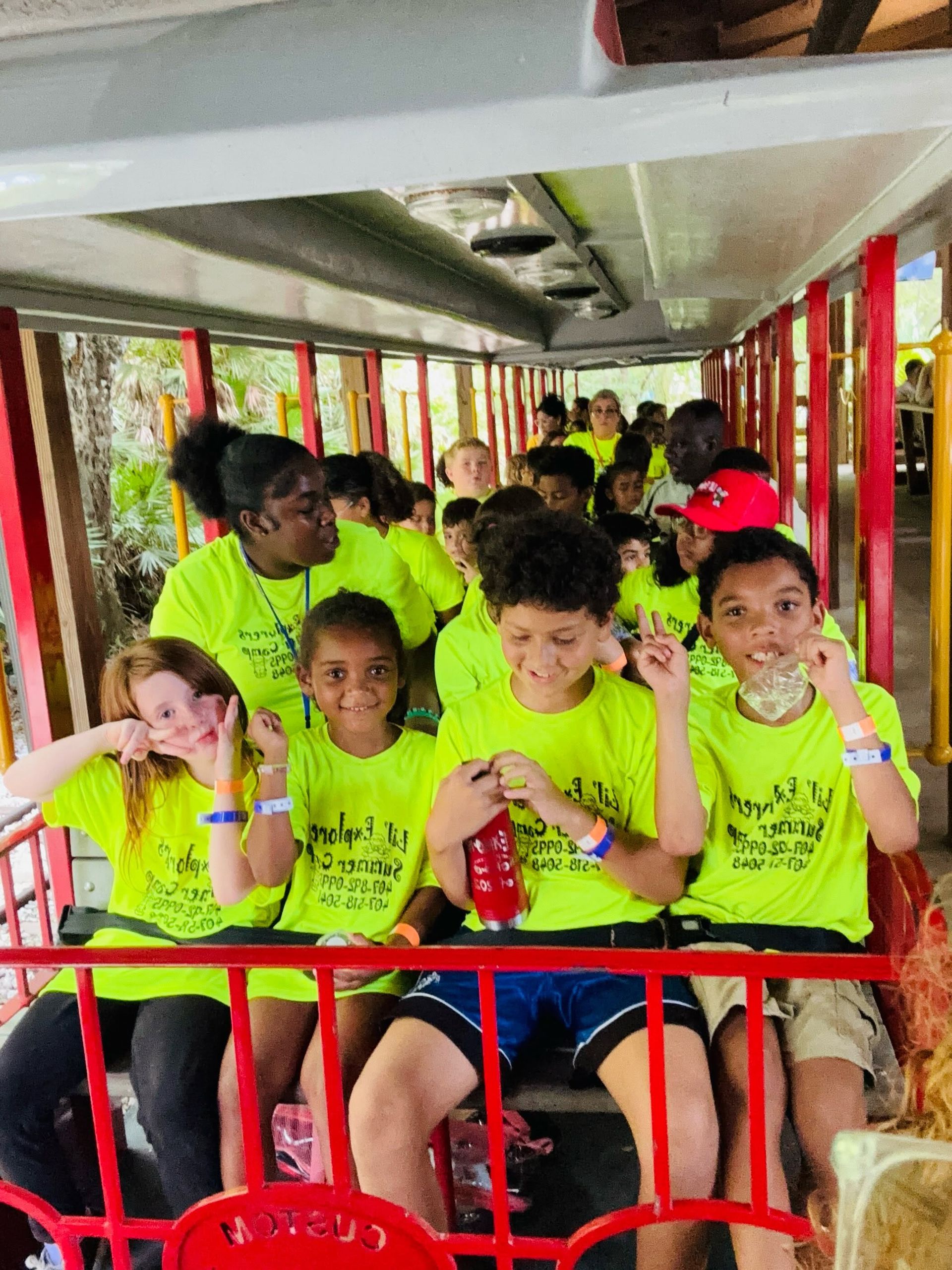 Children in neon yellow shirts sitting on a bus, holding snacks and smiling at the camera