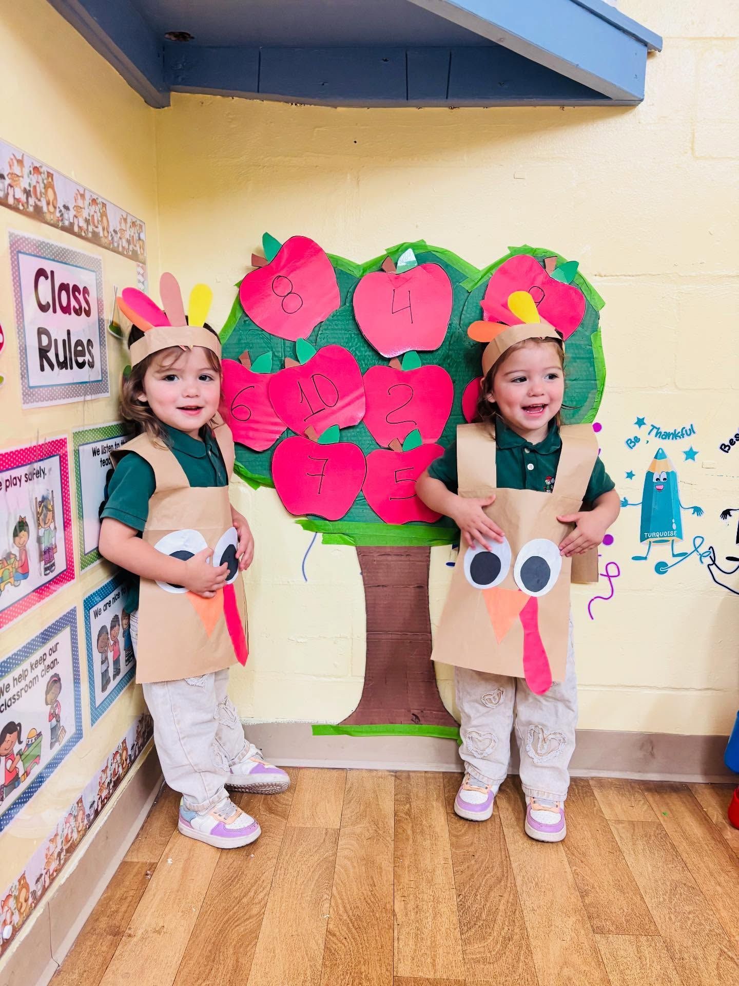 Two children in paper tree costumes standing by a colorful classroom tree display