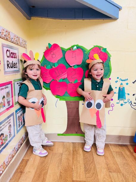 Two children in paper tree costumes standing by a colorful classroom tree display