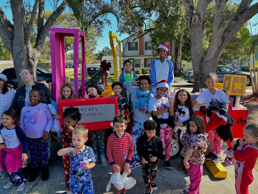 Group of children posing outdoors with colorful parade props and costumes under trees