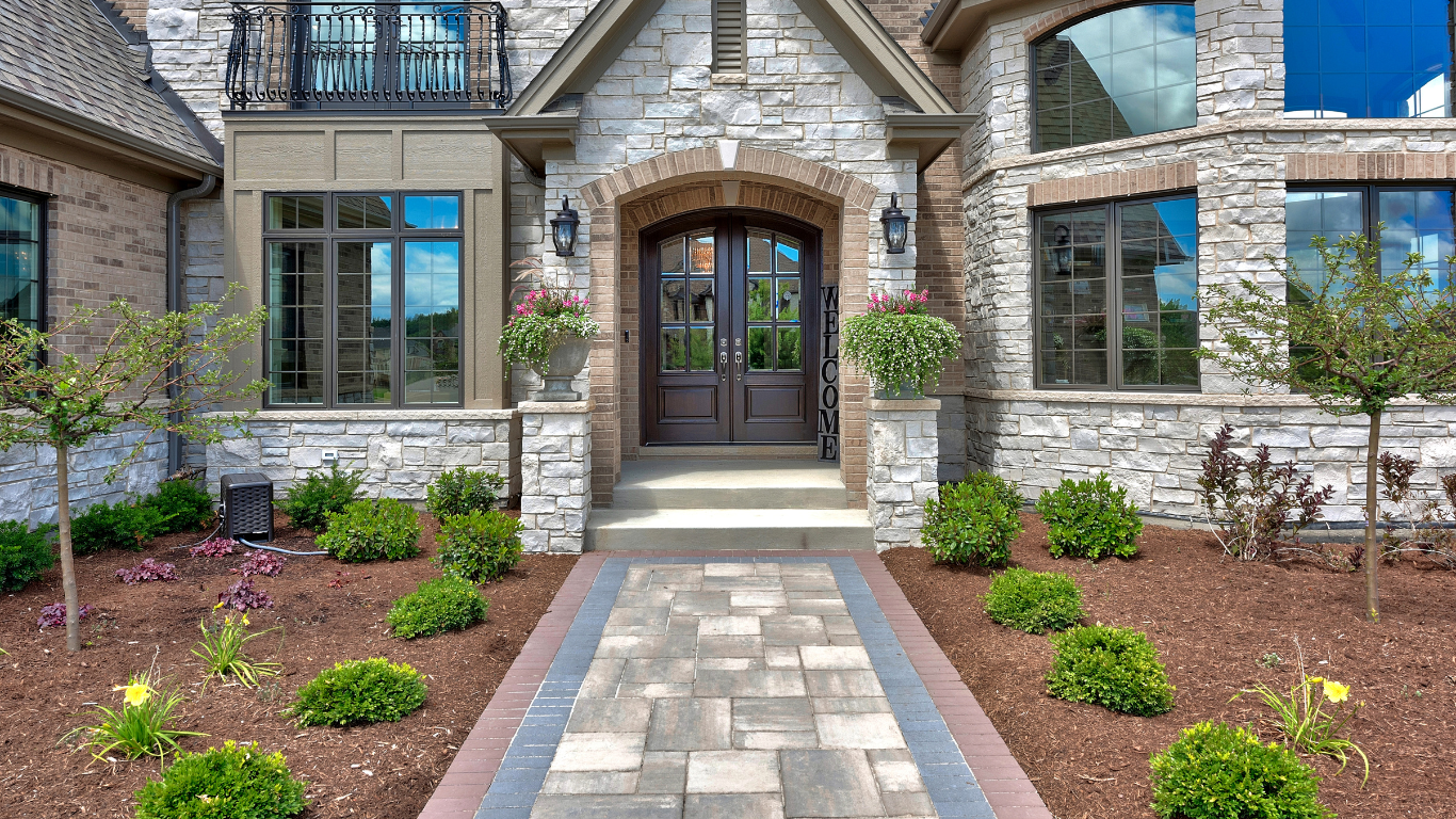 Stone facade entry with double doors, arched entrance, brick pathway lined with shrubs.