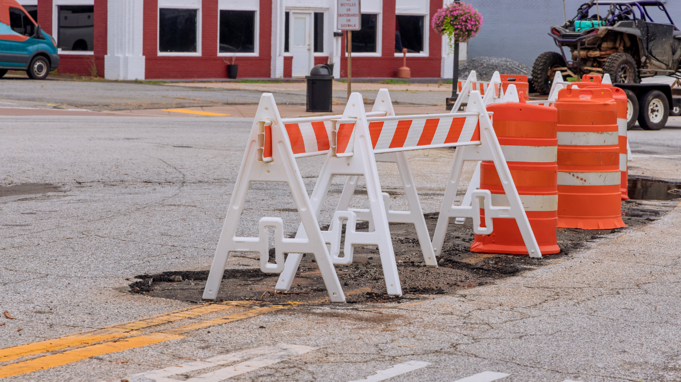 Road repair with white and orange barriers blocking off a damaged street in a town square.