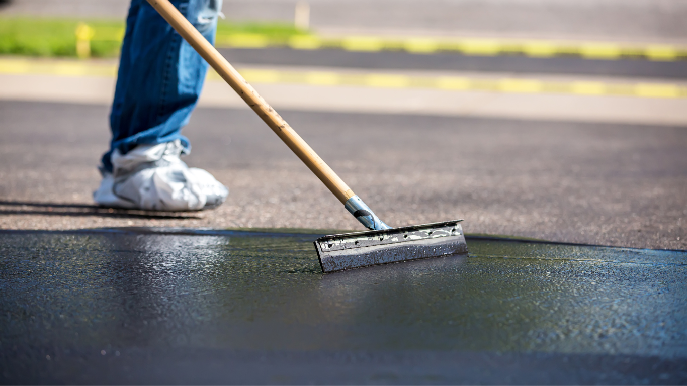 Person applying black sealant to asphalt with a squeegee.