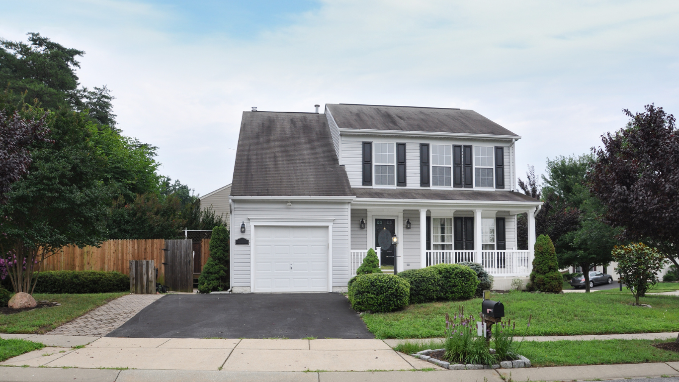 Two-story white house with black shutters, gray roof, and a small front porch, framed by trees and lawn.