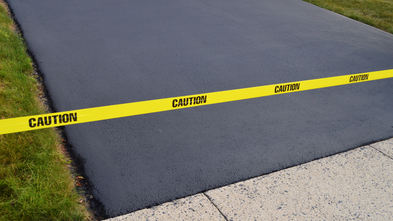 Freshly paved asphalt driveway with yellow caution tape.