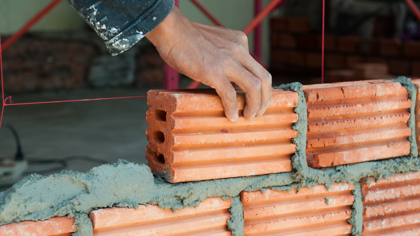 Hand placing a red brick onto a bed of mortar during construction of a brick wall.