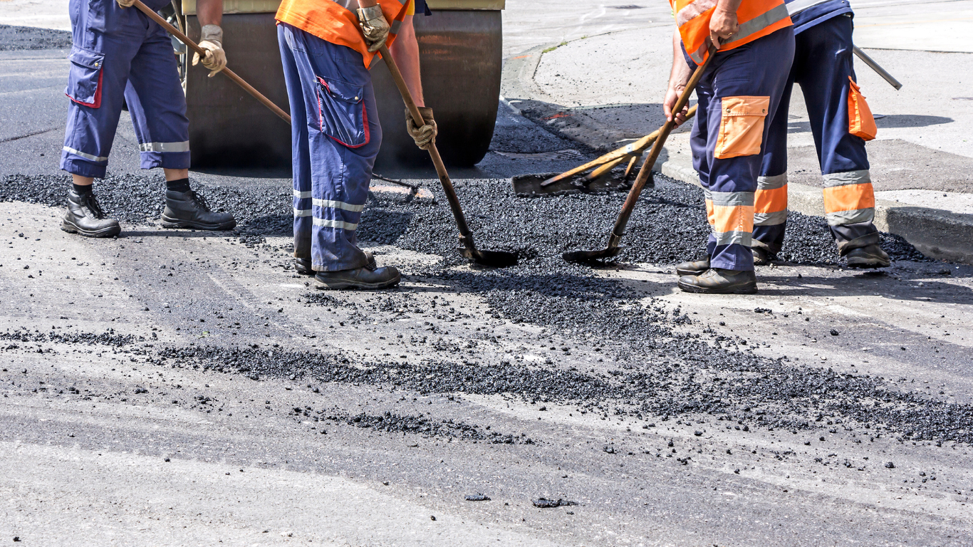 Road crew paving asphalt; workers rake and smooth dark pavement.