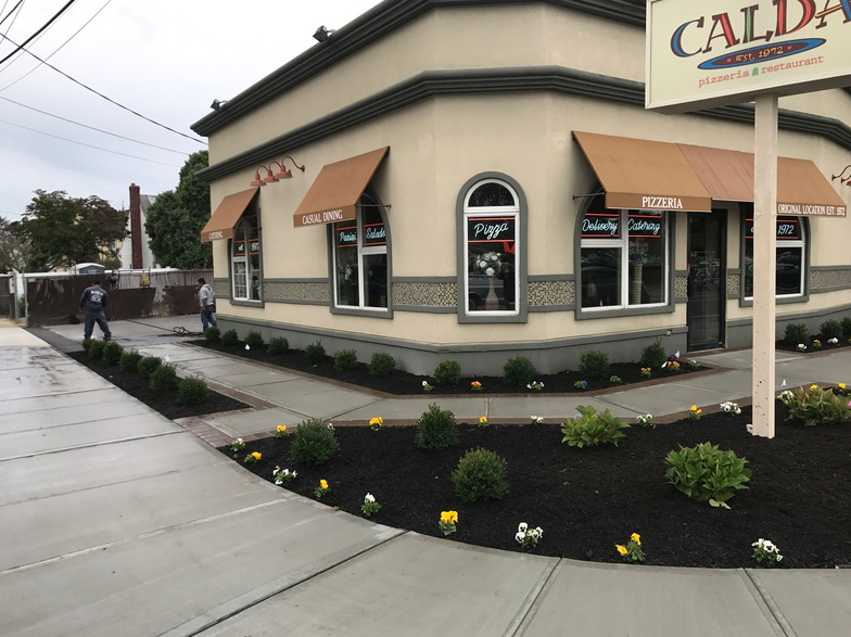 Corner building with tan exterior, brown awnings, and landscaping. Sign reads 