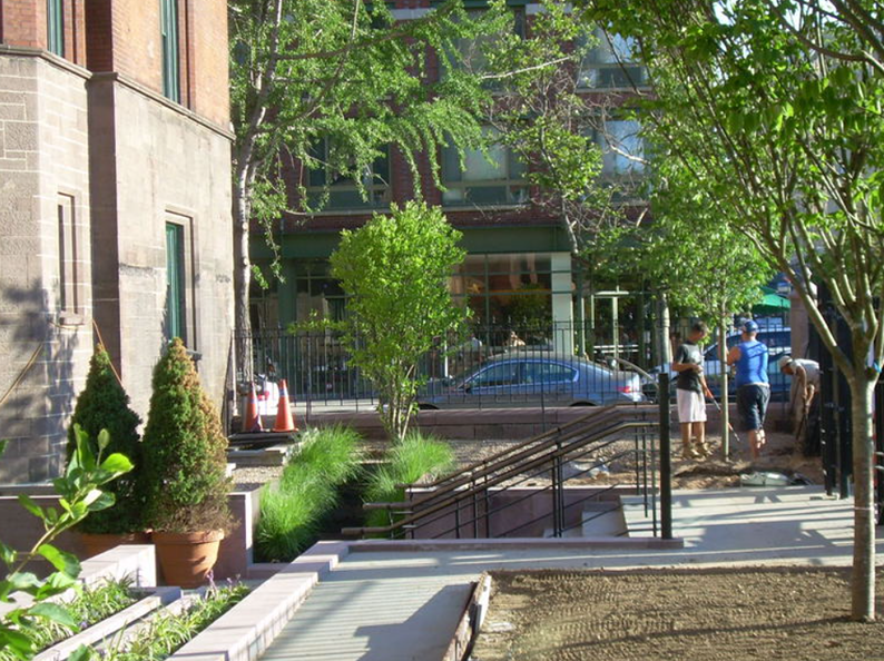 Exterior view of a landscaped area with trees, stairs, and people on a sunny day.