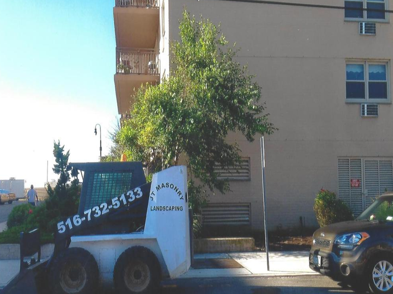 White and black Bobcat with phone number parked near a building with a tree.