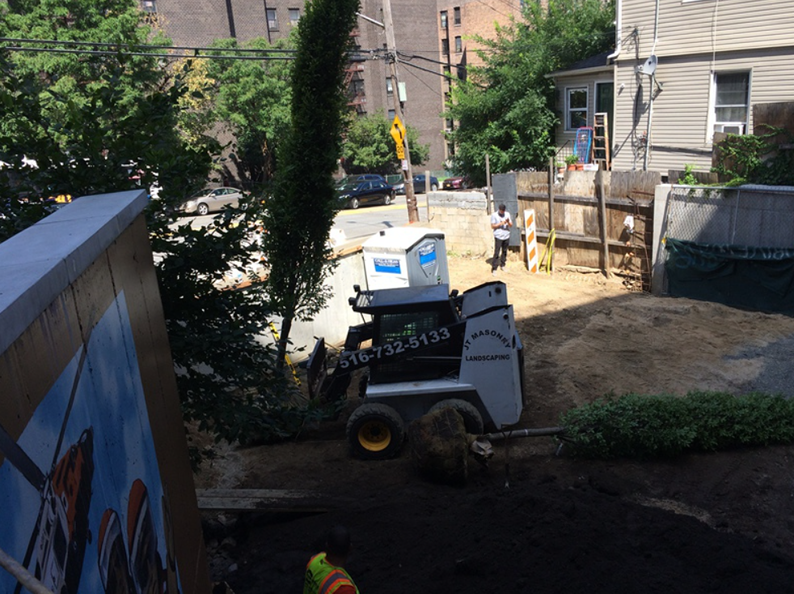 Bobcat tractor on a construction site with workers and a portable toilet.
