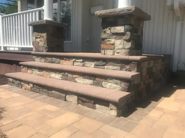 Stone steps leading to a home's entrance, with pillars flanking the doorway and a paved walkway.
