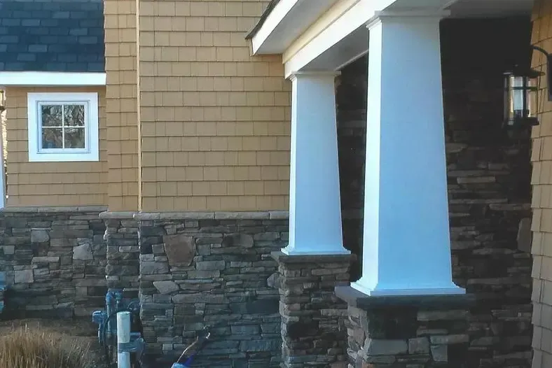 Beige and stone house exterior with white columns and a lit sconce.