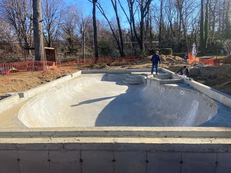 A concrete pool under construction, a person stands inside. Trees in background.
