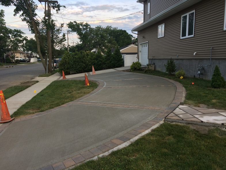 Concrete driveway curves toward a two-story home. Cones line the sidewalk.