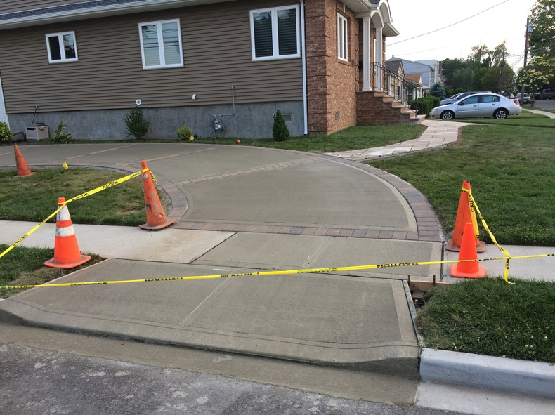 Freshly poured concrete driveway with orange cones and caution tape, in front of a house.