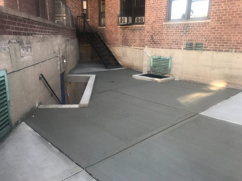 Newly poured concrete patio next to a brick building with a stairwell and basement entrance.