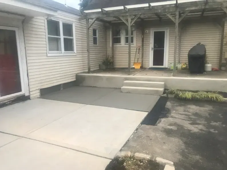 Concrete patio with steps, ramp, and adjacent house with a door.