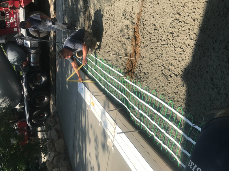 Workers placing green tubes in wet concrete for a construction project.