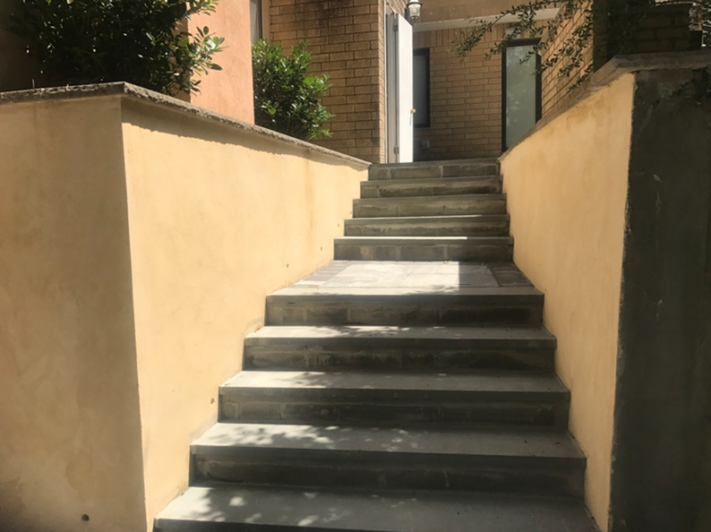 Concrete steps leading up, flanked by yellow walls. Sunlight and shadows on the steps.