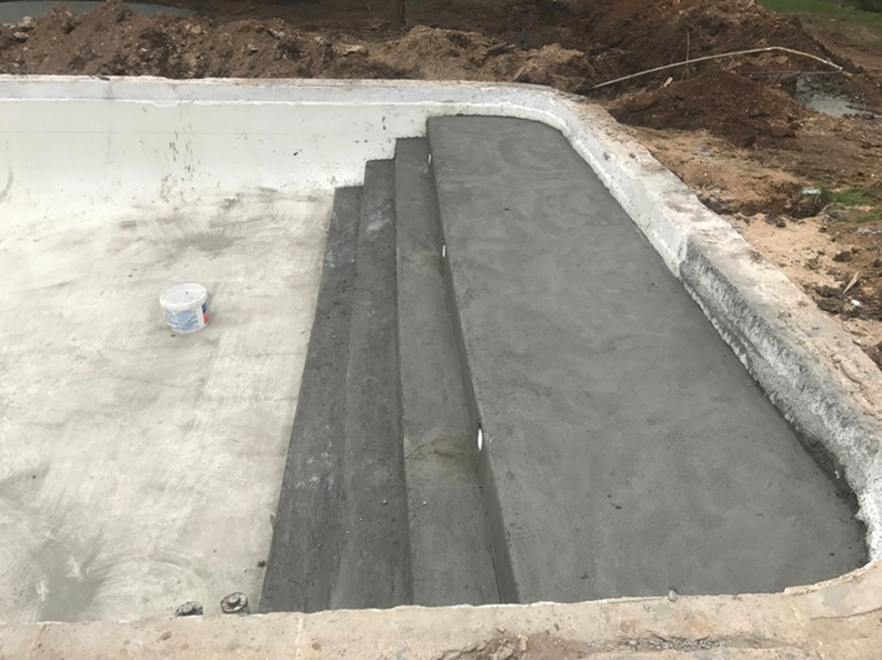 Concrete pool under construction with steps and a ramped entry.