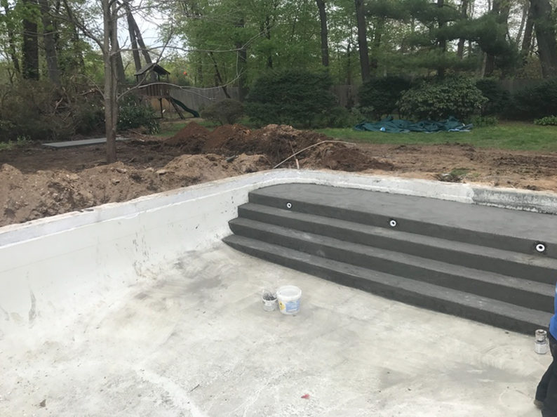 Pool under construction, concrete steps, gray, white, and tan tones, outdoor setting, dirt piles.