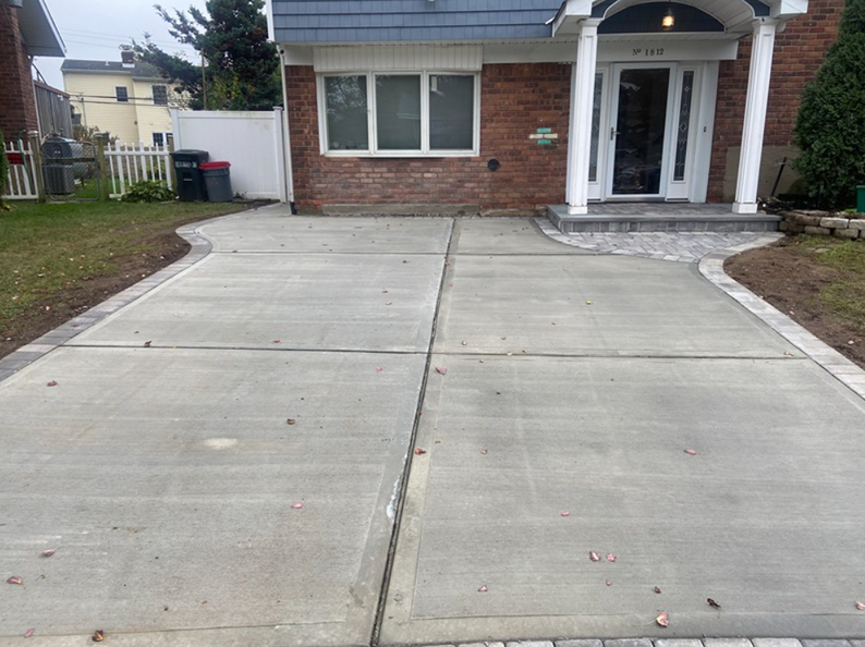 Concrete driveway leading to a brick house with a white door and a paved walkway.
