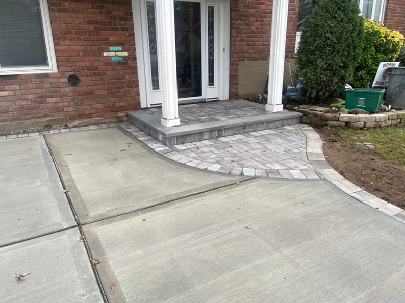 Brick house with a concrete driveway leading to a paved entrance.