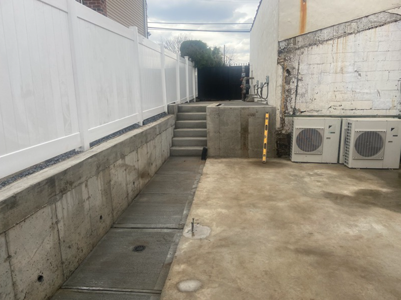 Concrete path, stairs, and white fence next to a building with AC units.