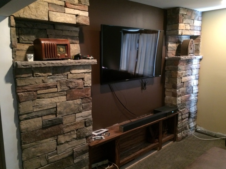 Stone accent wall with built-in shelves, holding a TV, radio, and media console. Brown and beige tones.