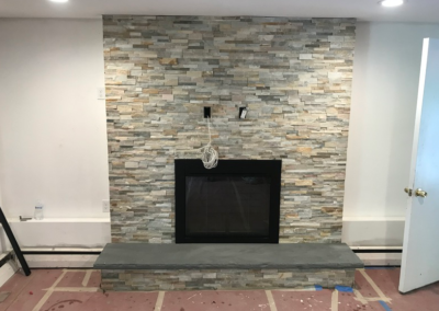 Fireplace with stone surround, black firebox, gray hearth. Walls are white and the floor is pink.
