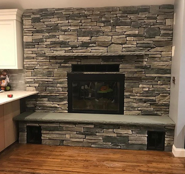 Stone fireplace with gray and beige stones, black fireplace insert, and wooden floor.