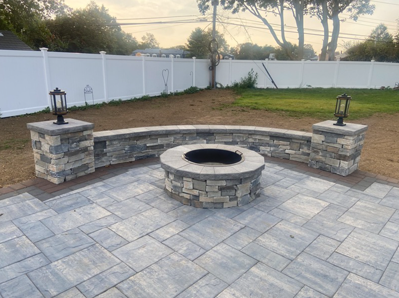 Stone patio with fire pit, curved wall seating, and lamppost pillars, backyard.