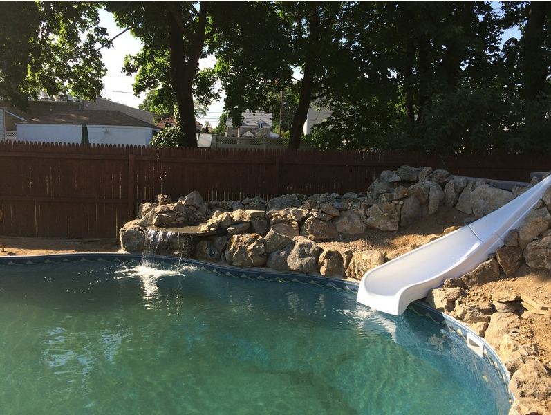 Swimming pool with a slide, waterfall, and rocky landscaping in a backyard.