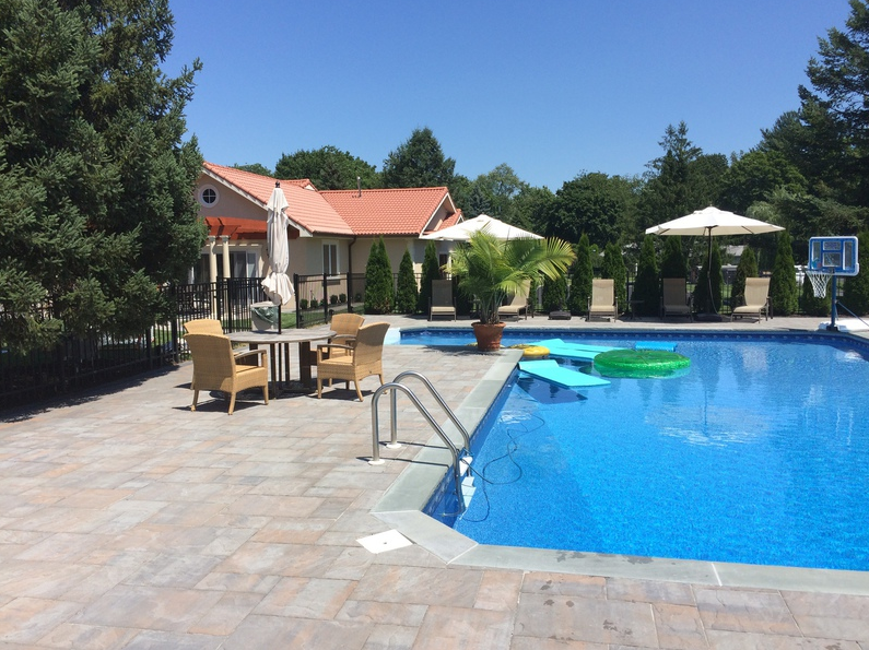 Swimming pool with lounge chairs, umbrellas, and a house in the background on a sunny day.