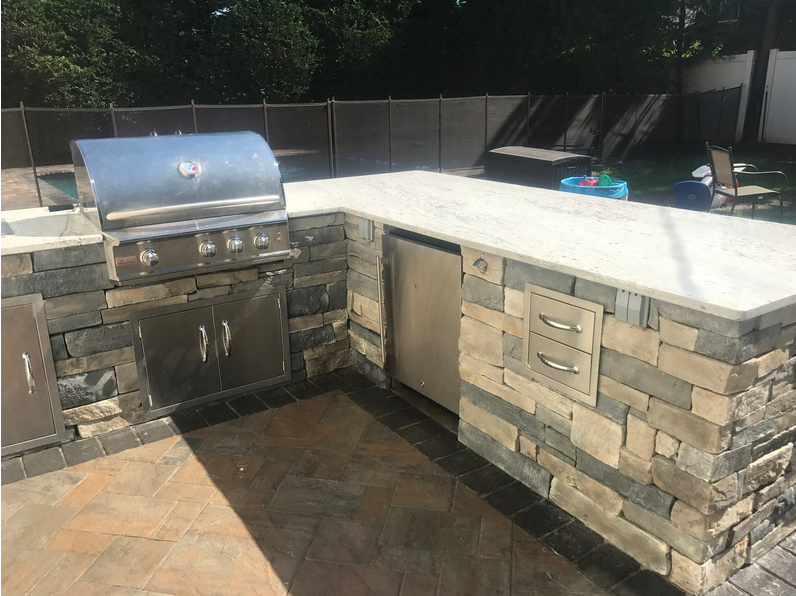 Outdoor kitchen with stainless steel appliances, stone facade, and concrete countertop.