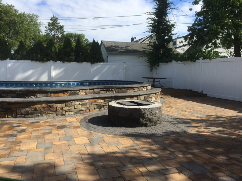 Backyard with pool, fire pit, and paver patio against a white fence.