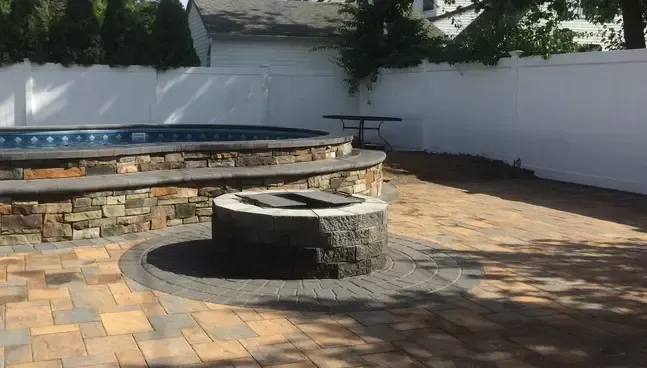 Backyard with pool and stone fire pit, surrounded by a brick patio and white fence.