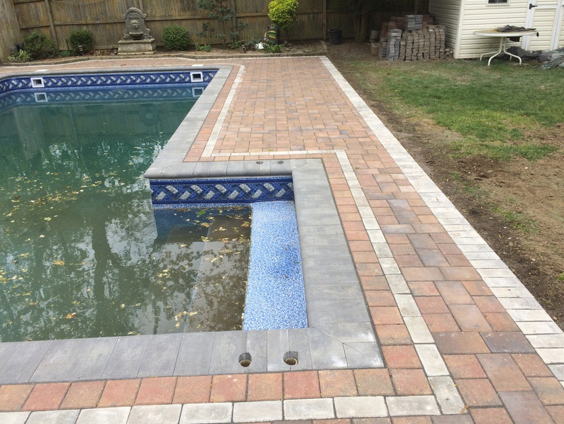 Brick patio surrounds a pool with blue tile and light-colored paving.