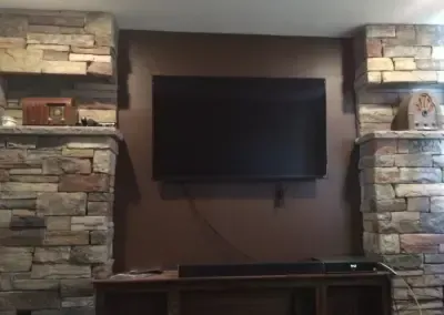 TV mounted on brown wall between stone columns; soundbar below.