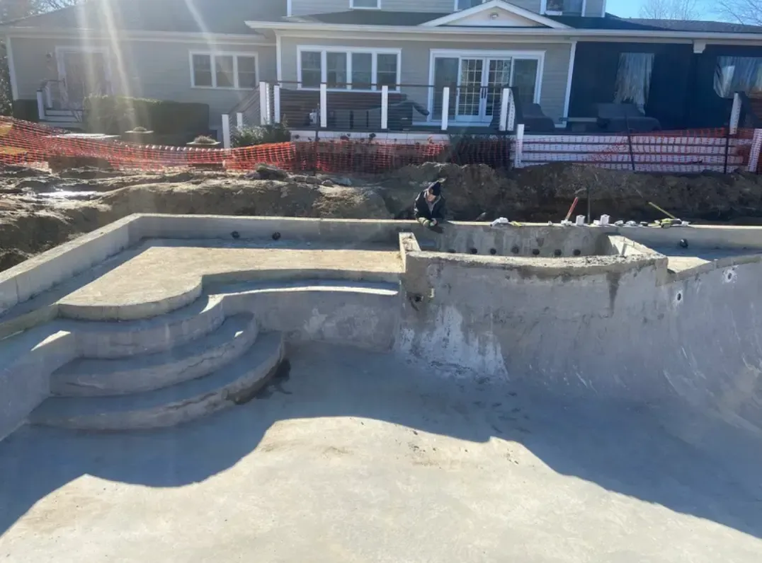 Concrete swimming pool under construction with steps, against a house.