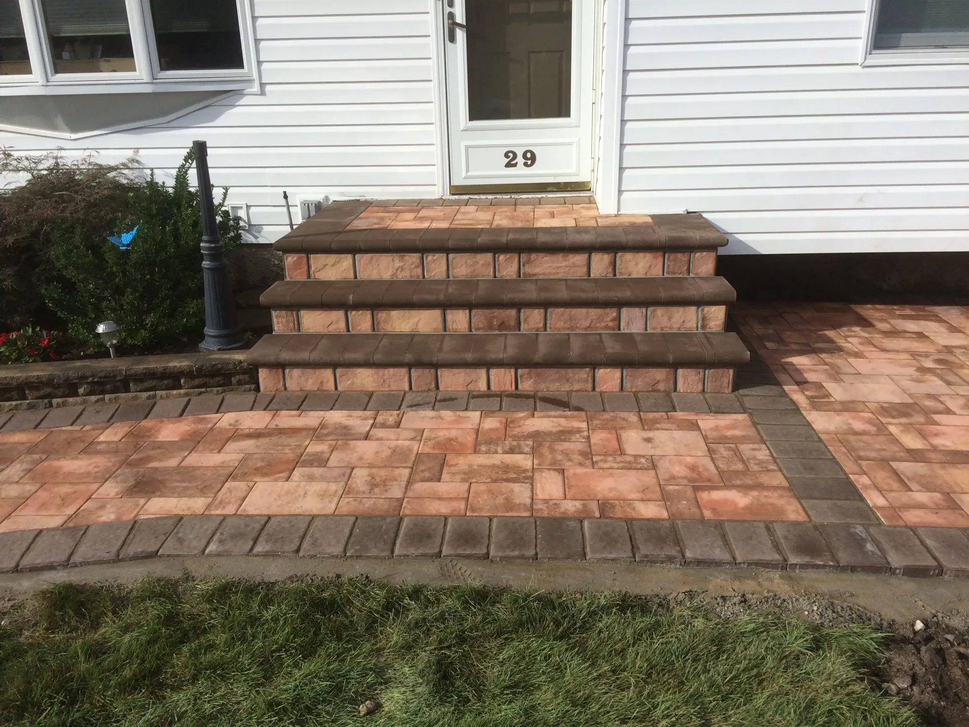 Brick steps leading to a white door with a brick walkway, all in shades of brown and tan.