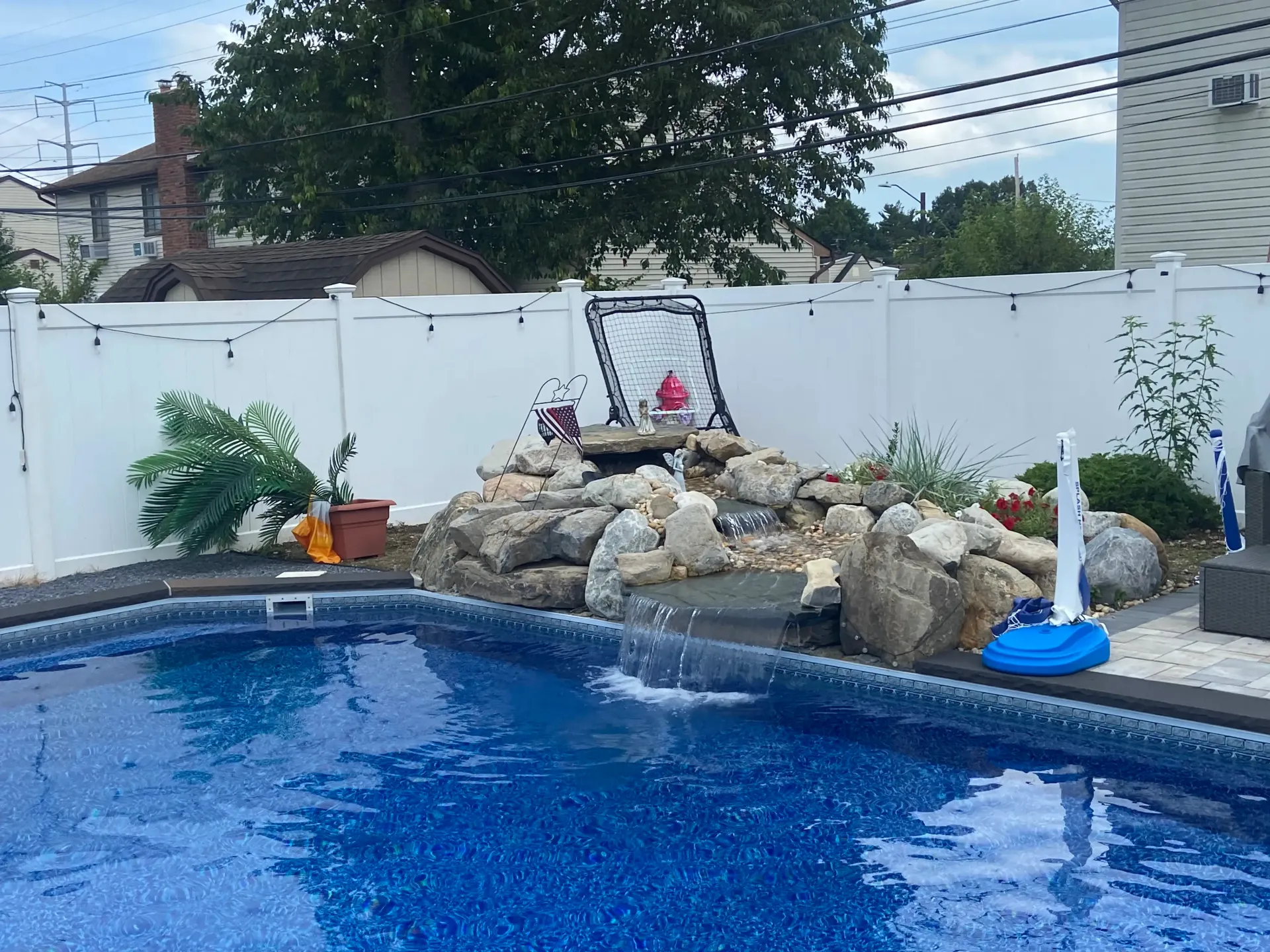 A backyard pool with a waterfall feature. White fence, blue water, and rocks.