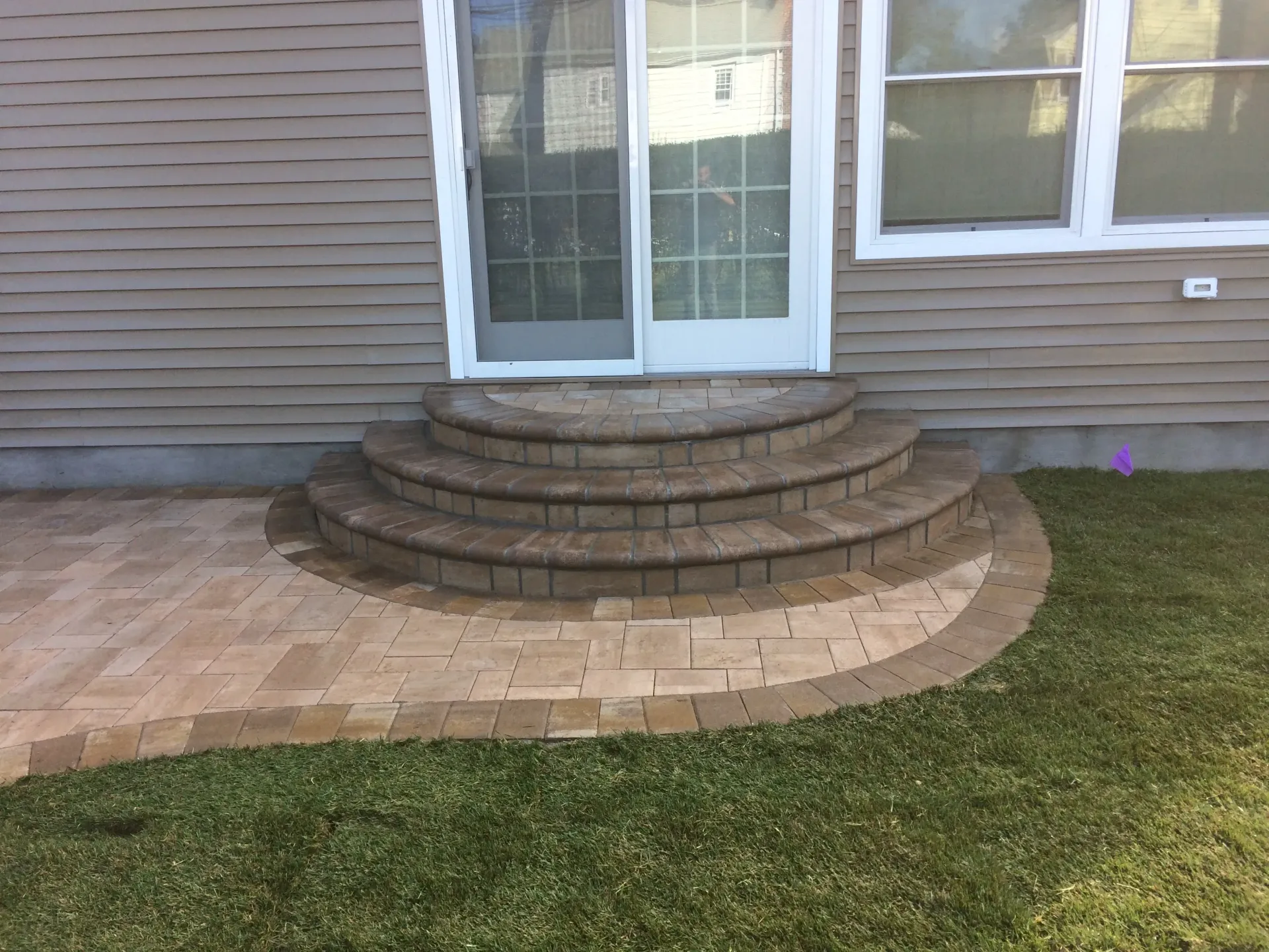 Brick steps leading to a sliding glass door on a beige siding house. Brick patio and green grass surround.