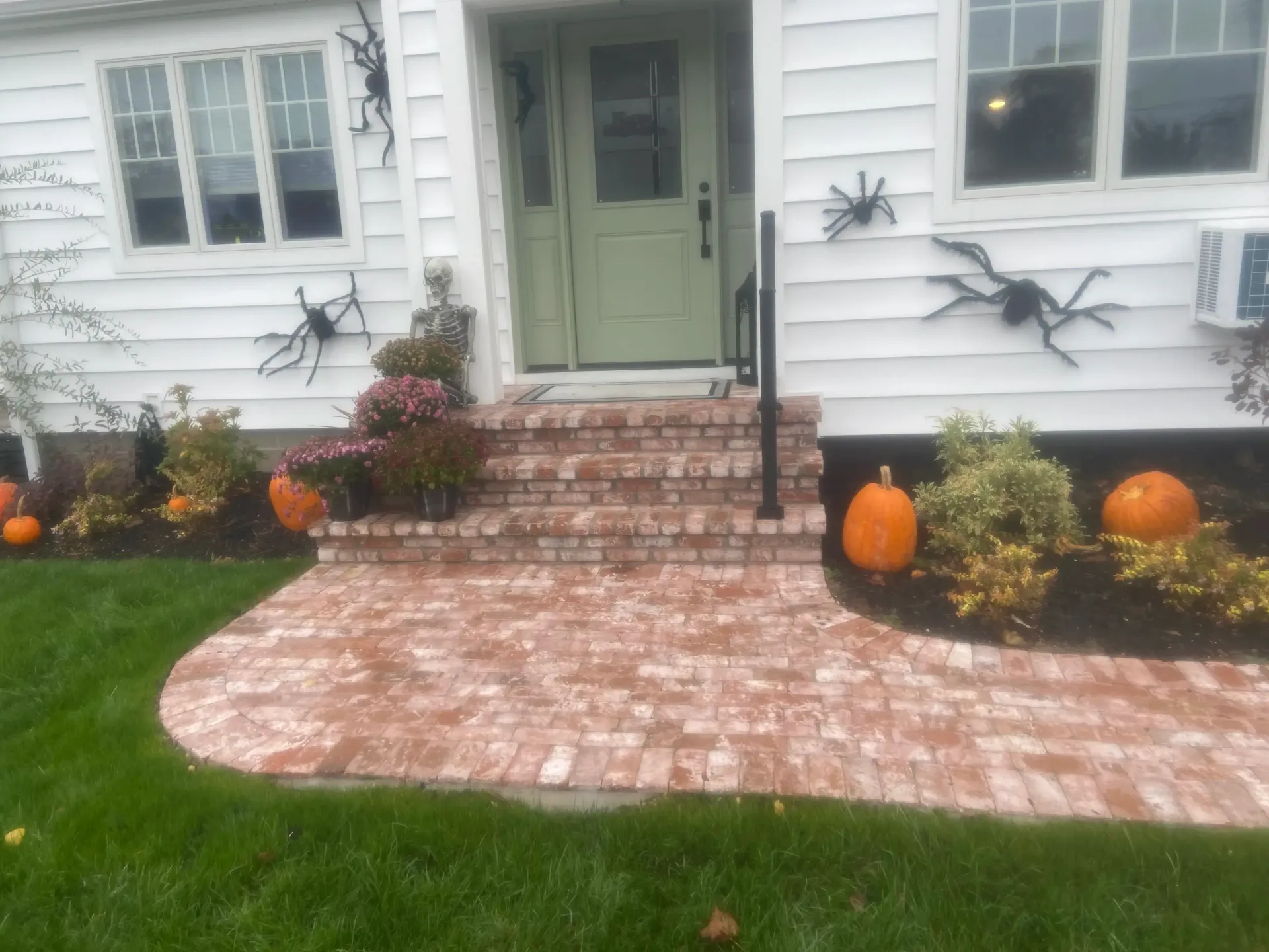A white house decorated for Halloween with pumpkins, spiders, and brick steps leading to a green door.